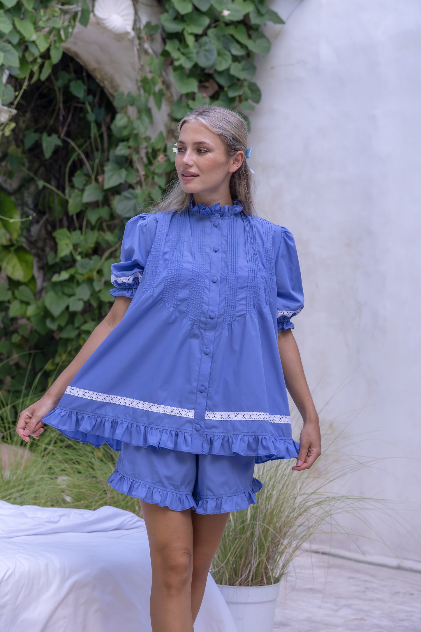 Close up of Alma Bluebell babydoll blouse in cornflower blue organic cotton showing white lace cuff trim, pintuck bib detail and covered button placket