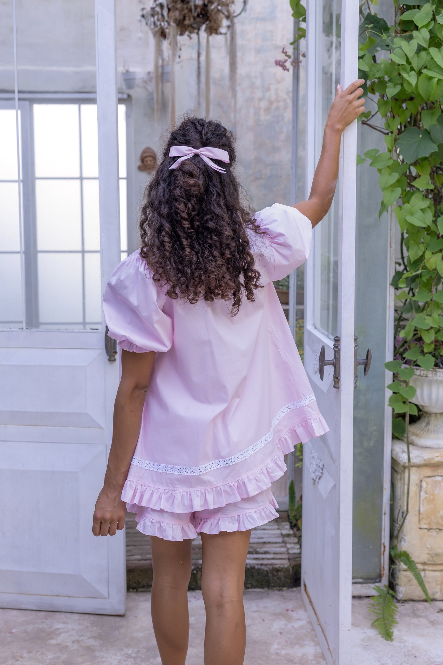 Woman in a pink Love Letters x Alma Blossom organic cotton set standing in a doorway with plants around.