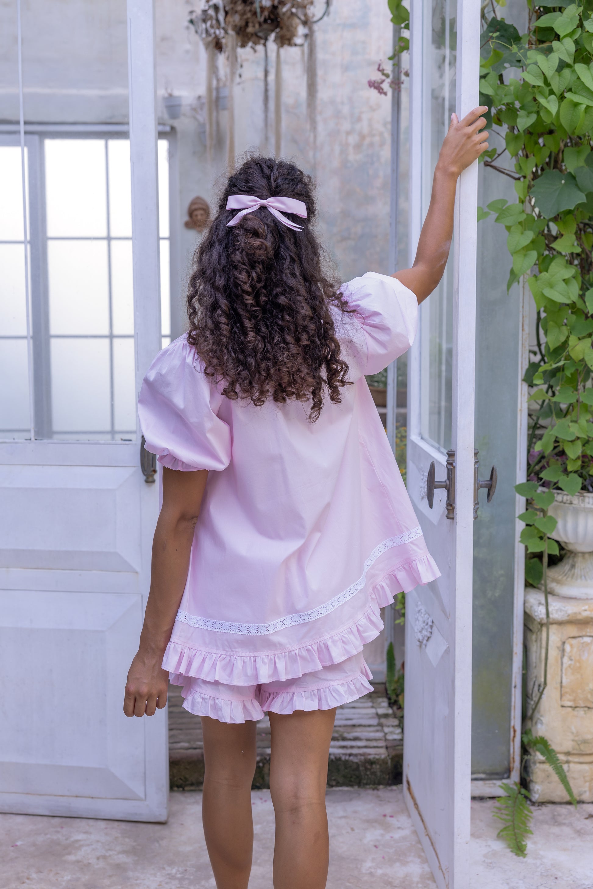 Woman in a pink Love Letters x Alma Blossom organic cotton set standing in a doorway with plants around.