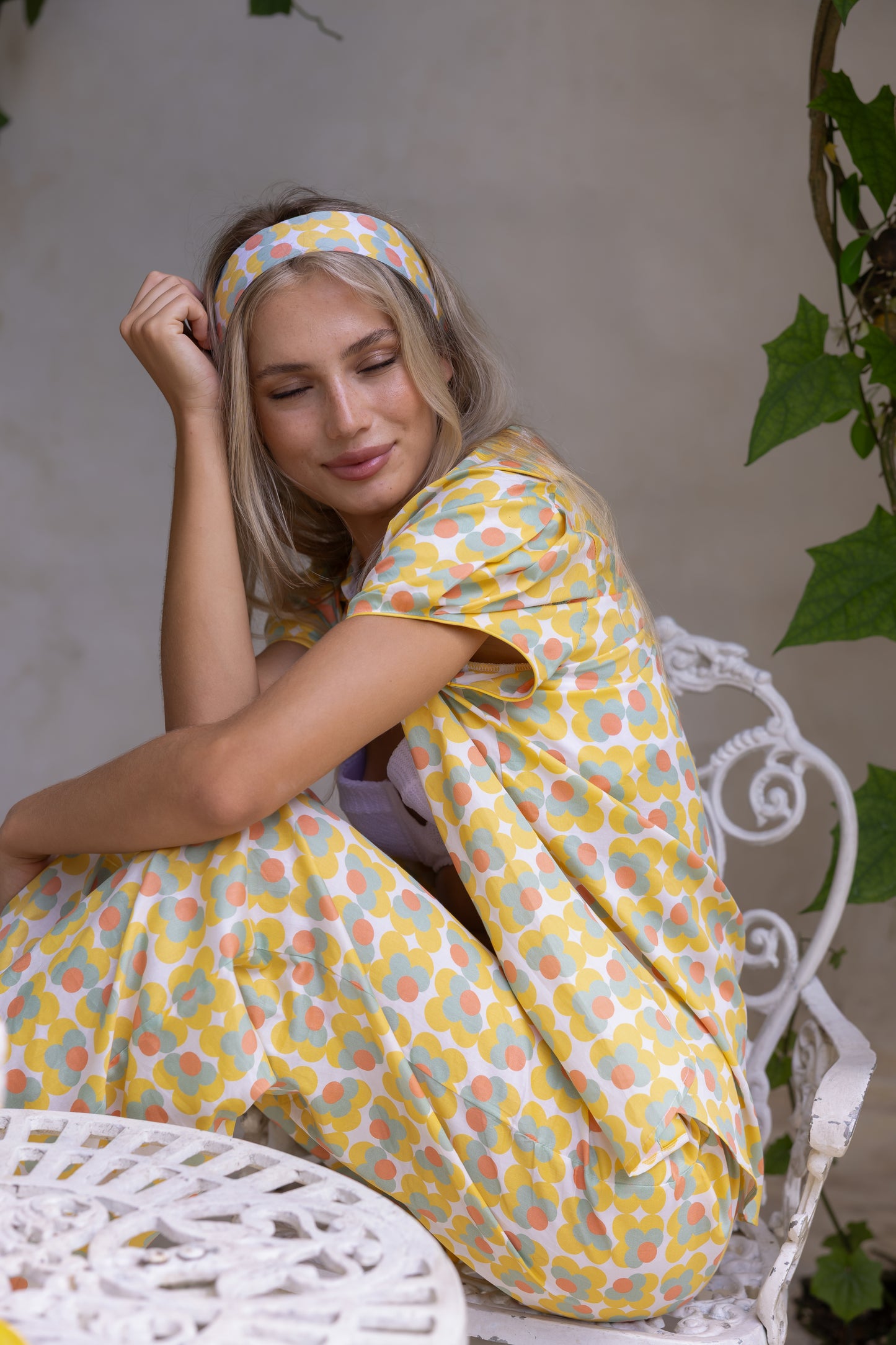 Woman wearing a yellow patterned dress sitting on a white chair outdoors.